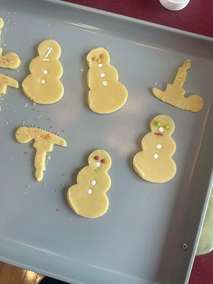 Unbaked snowman and festive shape sugar cookies arranged on a baking sheet, showcasing a funny r/bakingfail.