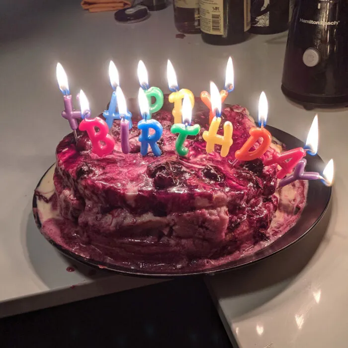 A homemade birthday cake covered in berry jam and lit candles as a funny baking fail.