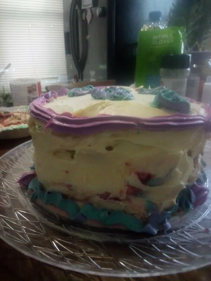 Unevenly frosted homemade cake with purple and teal icing on a platter, showing a bakingfail.