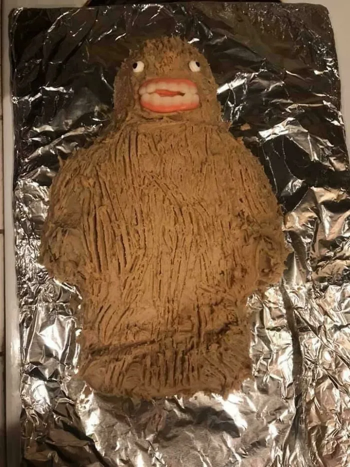 A funny baking fail featuring a brown Bigfoot shaped cake decorated with candy teeth and eyes.
