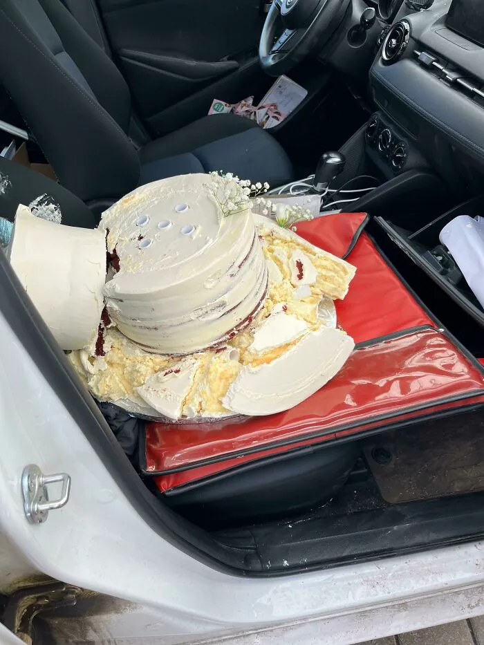 A major baking fail showing a multi-tiered white frosted cake smashed inside a car.