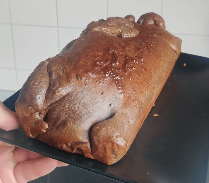 A funny baking fail displaying a dark brown, dense loaf of bread served on a black tray.