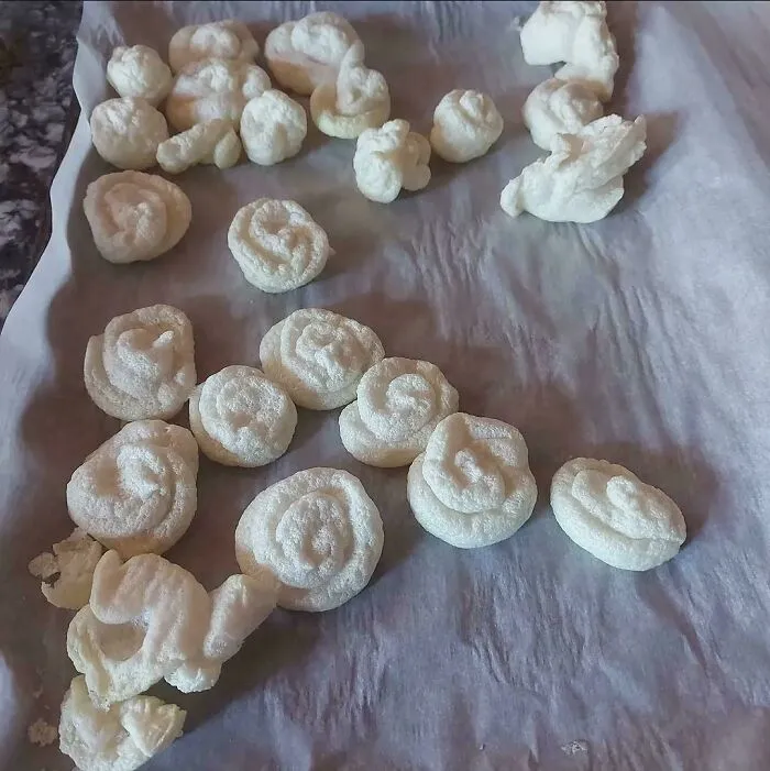 An amusing baking fail showing pale, irregular meringue-like swirls scattered on parchment paper.