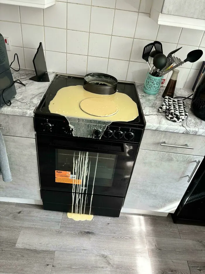 A major baking fail with liquid cake batter spilled over a stovetop, oven door, and floor.