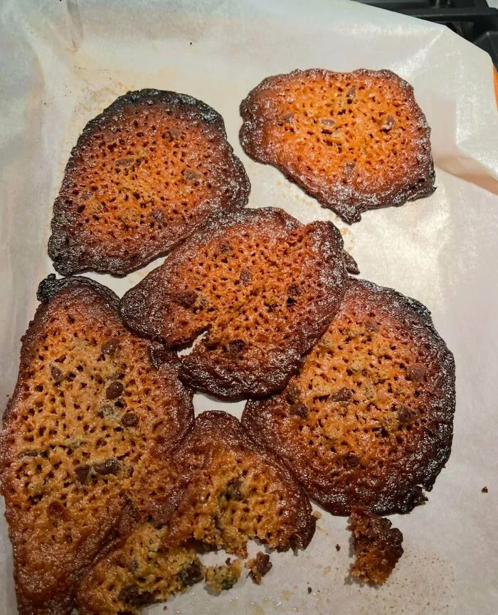 A baking fail featuring overbaked, flat, lace-like burnt cookies spread out on baking paper.