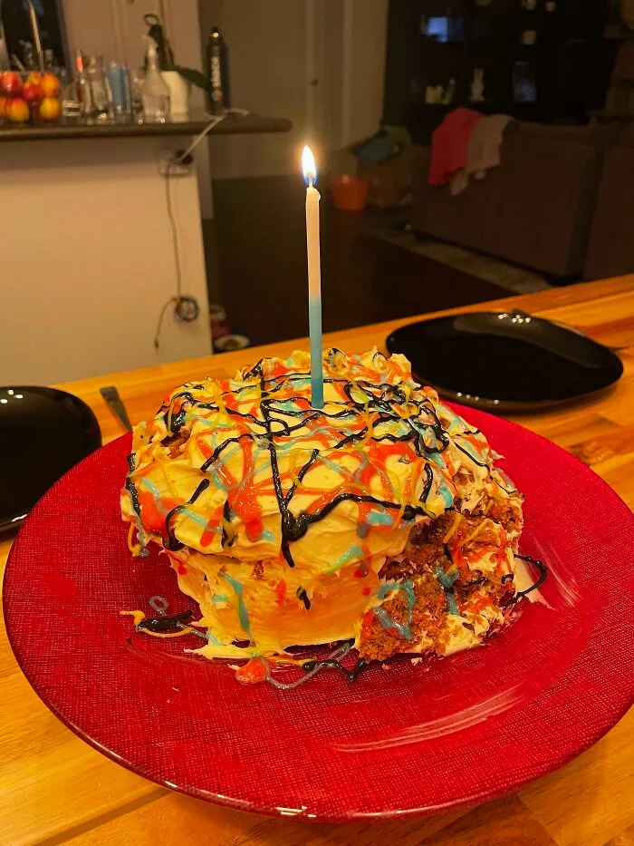 A messy colorful birthday cake on a red plate, demonstrating a funny bakingfail.