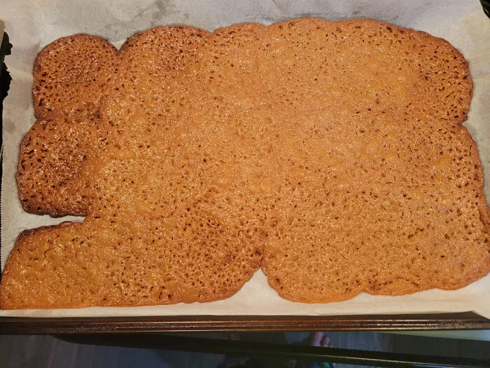Overly spread cookies fused into one large sheet on parchment paper, a clear baking fail