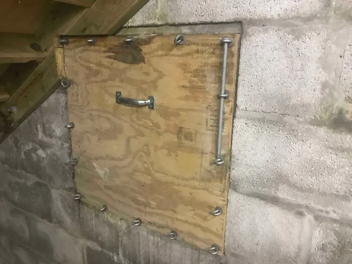 Cursed images displaying a heavily bolted plywood door sealed into a concrete basement wall