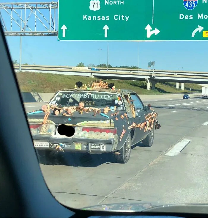 Car covered in plastic dolls and strange objects driving on highway, an example of cursed images.