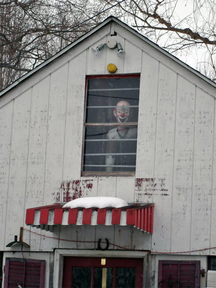 Cursed images of a scary clown mannequin staring out of an upper floor window of a white barn