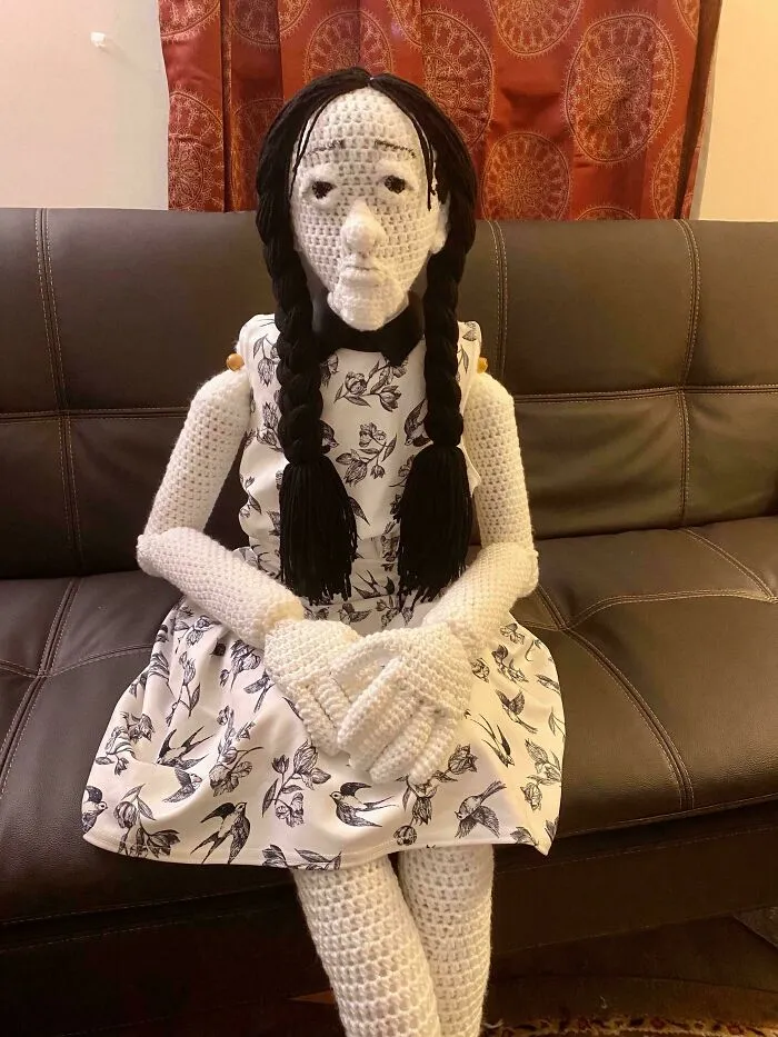 A creepy life-sized knitted doll sitting on a brown leather couch, listed in cursed images.