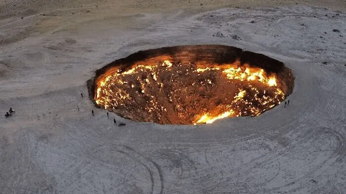 An aerial view of the fiery Darvaza gas crater burning intensely in the desert, representative of cursed images.