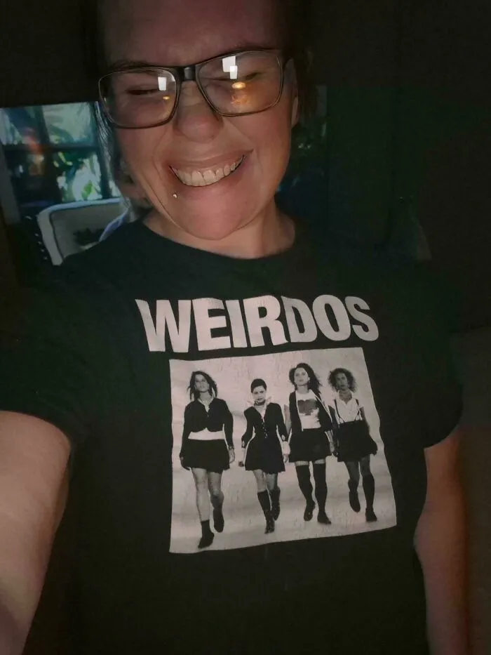 A smiling woman wearing a t-shirt featuring a spooky design, adding to a collection of creepy photos.