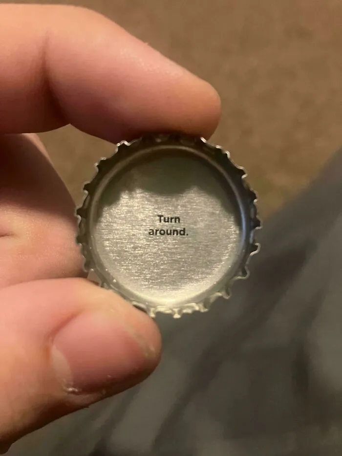 A bottle cap held in a hand reading Turn around inside, serving as one of many cursed images.