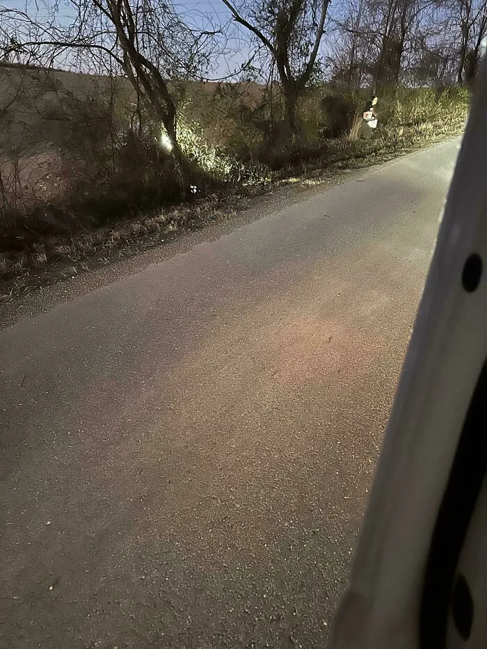 A dark country road at night with an unsettling figure in the distance, fitting creepy photos with no explanation.
