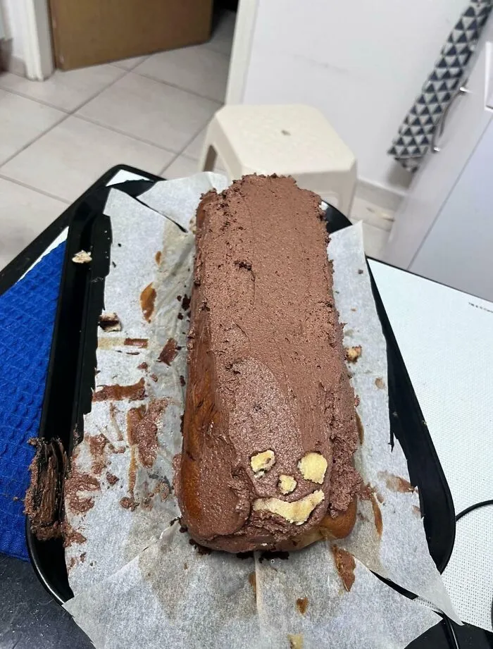 A funny baking fail featuring a chocolate covered loaf cake with a crude face drawn in frosting.