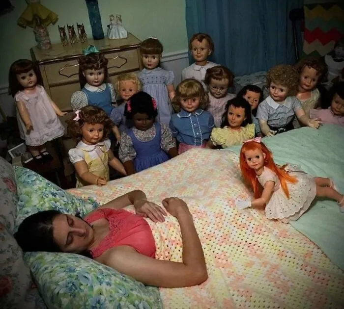 A woman sleeping surrounded by eerie vintage dolls gathered around her bed, evoking cursed images.