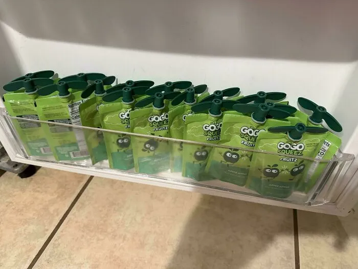 A refrigerator shelf neatly stocked with green applesauce pouches prepared by a dad for his kids snacks.