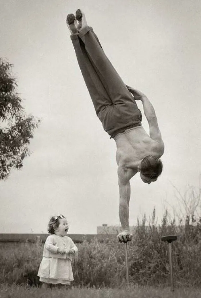 Vintage historical photo of a man performing handstand to impress a child
