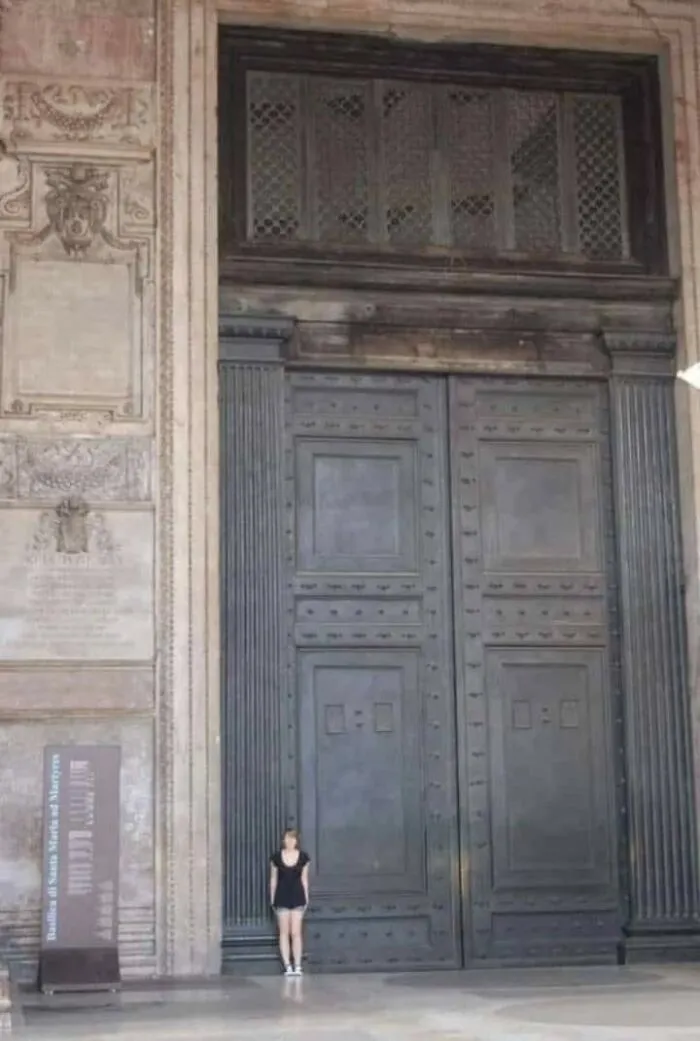 Rare historical photo showing a woman standing beside an enormous ancient door for scale