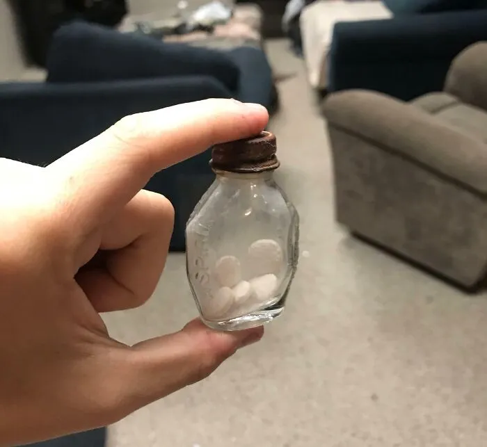 Hand holding a small vintage glass bottle with old pills inside