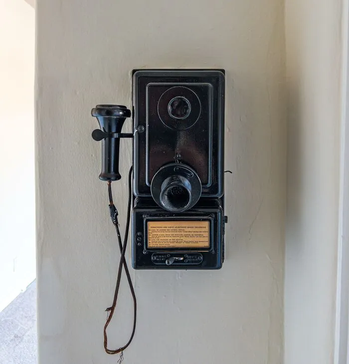 Black antique wall-mounted telephone with handset on beige wall