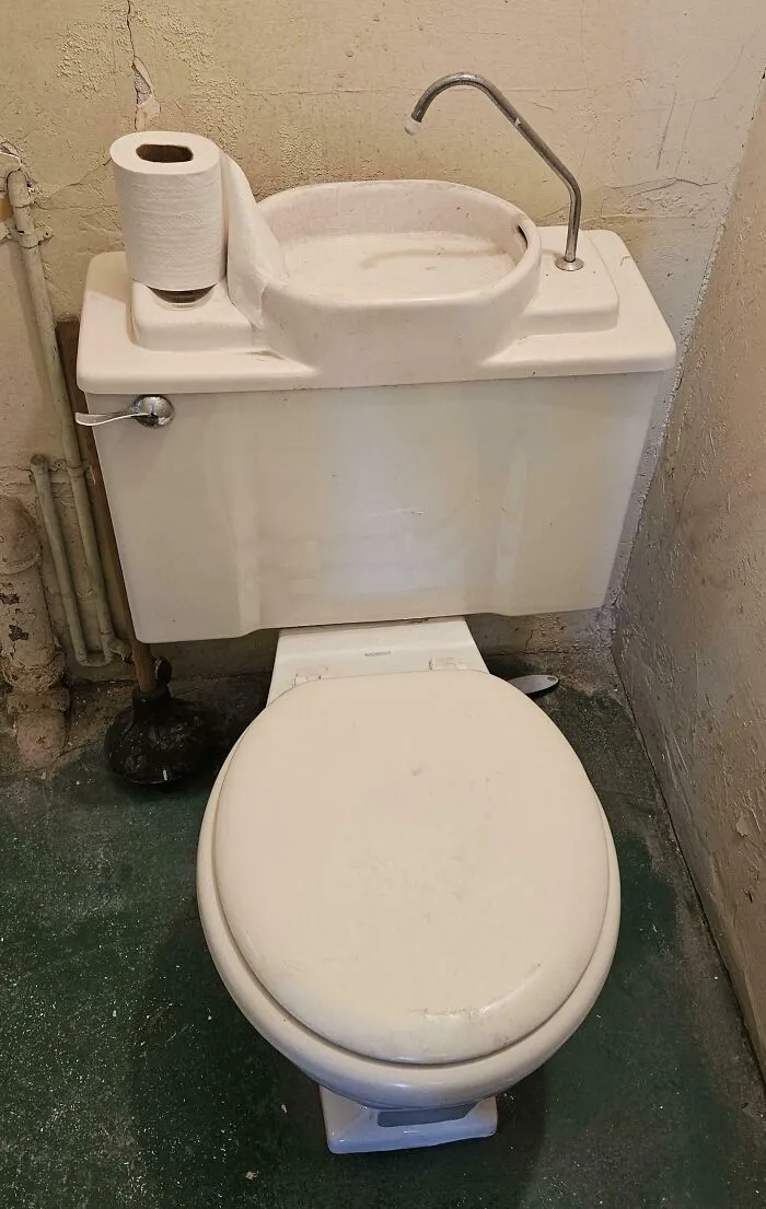 Old toilet with sink faucet attached on the tank in a worn bathroom