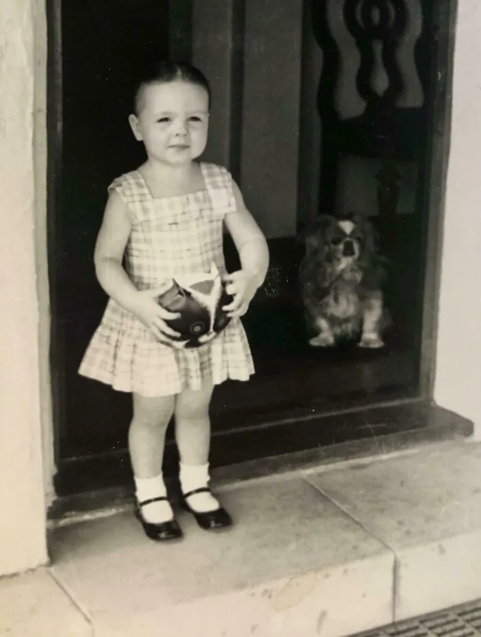 Vintage black and white photo of toddler girl standing with toy and dog
