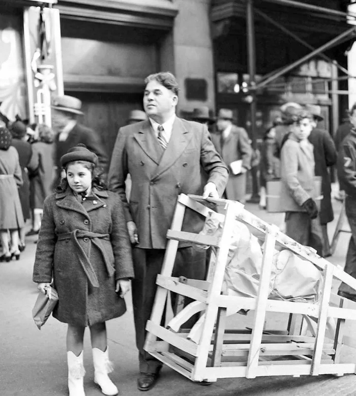 Rare historical photo of man and young girl carrying a large boxed item on busy street