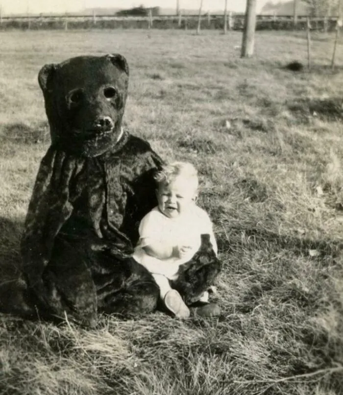 Rare historical photo of a baby sitting next to a person in a bear costume outdoors
