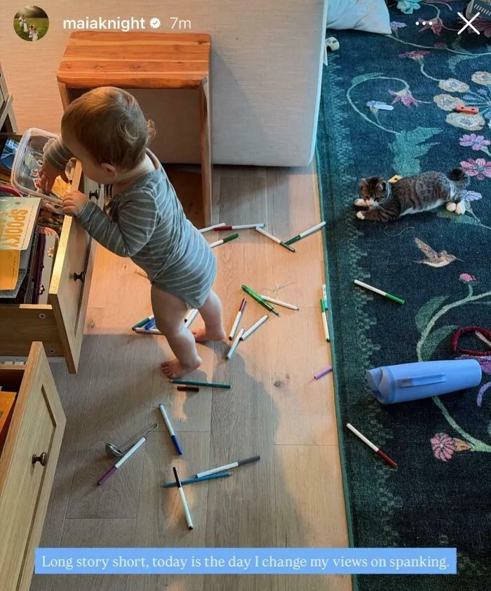 Toddler playing with scattered markers on floor with cat nearby and caption on spanking views
