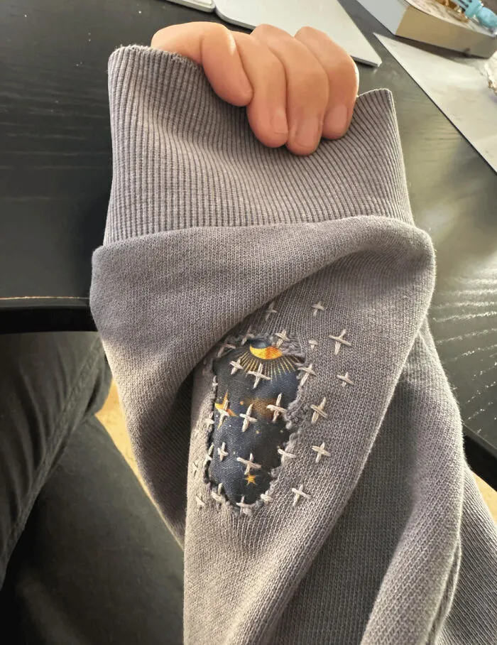 Person displaying a mended sweater sleeve with embroidered stars, showing a little creativity to save money.