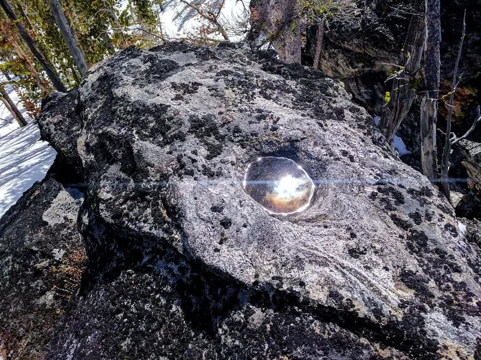 Sunlight reflecting from a water droplet on a dark rock surface