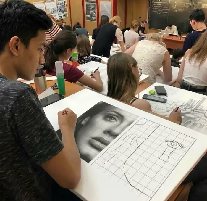 Art class student drawing a realistic face while another draws a simple doodle, captured in a funny photo.