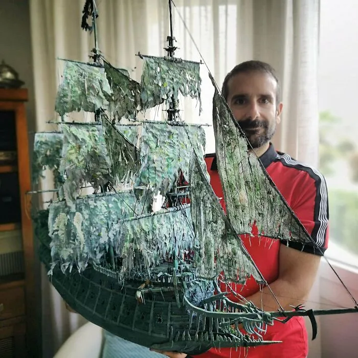 Man holding a large weathered miniature model of a tattered sailing ship
