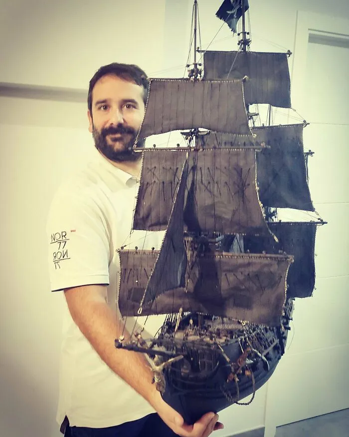 Man holding a large, detailed miniature model of a ship with black sails
