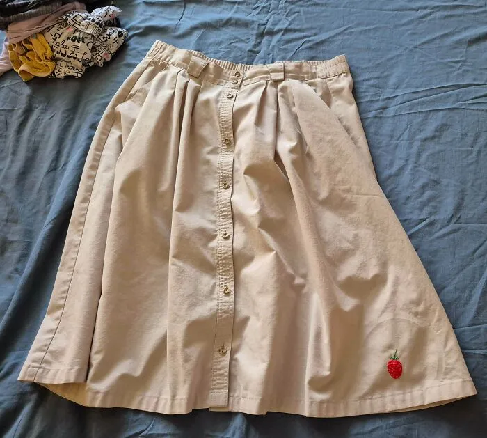 A beige button-up skirt with a small embroidered strawberry showing creativity that can save money.
