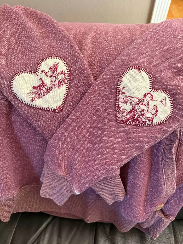 Heart patches repaired on a pink sweatshirt sleeves showing creativity to save money.