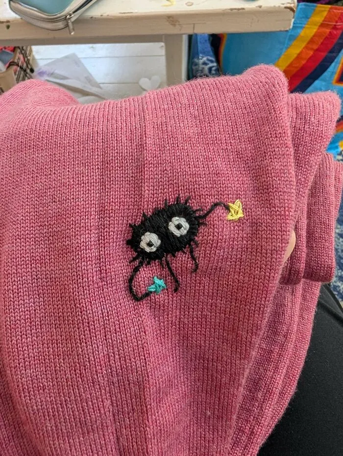 Small soot sprite embroidery on a pink sweater showing creativity to save money