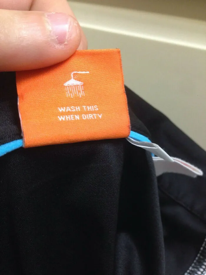 Orange shirt tag with confusing labels saying wash this when dirty under a shower icon.