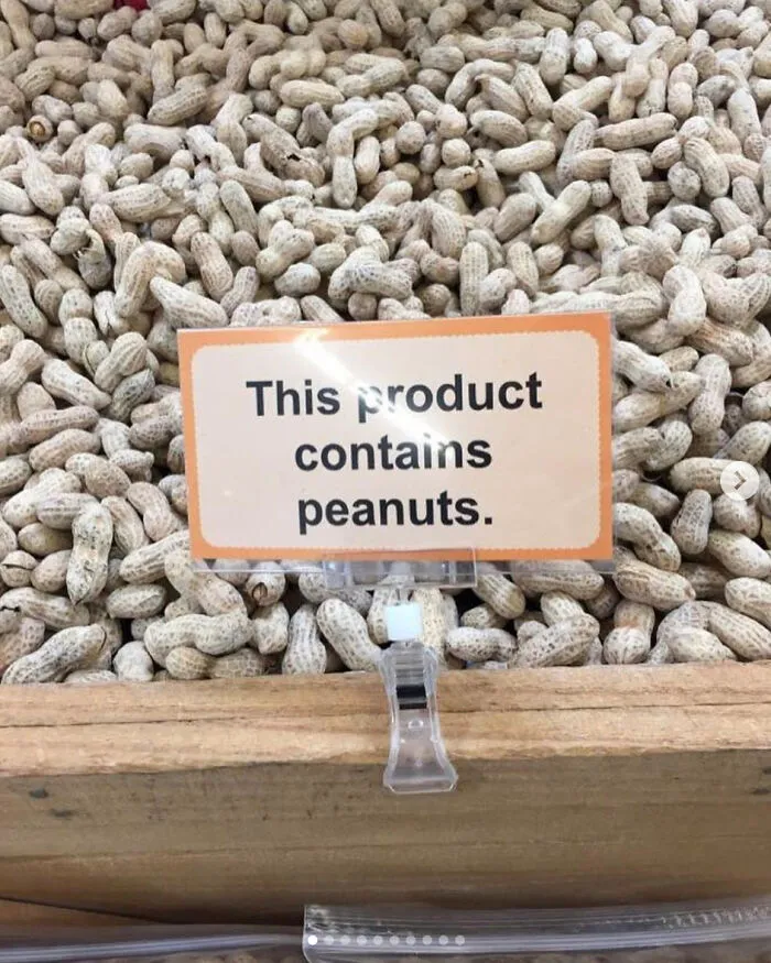 A sign placed in a bin of whole peanuts reading 'This product contains peanuts' as an example of confusing labels.
