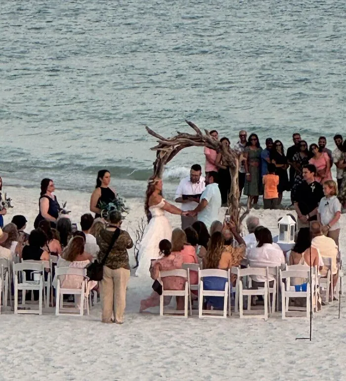 Beach wedding ceremony with guests seated and couple under wooden arch