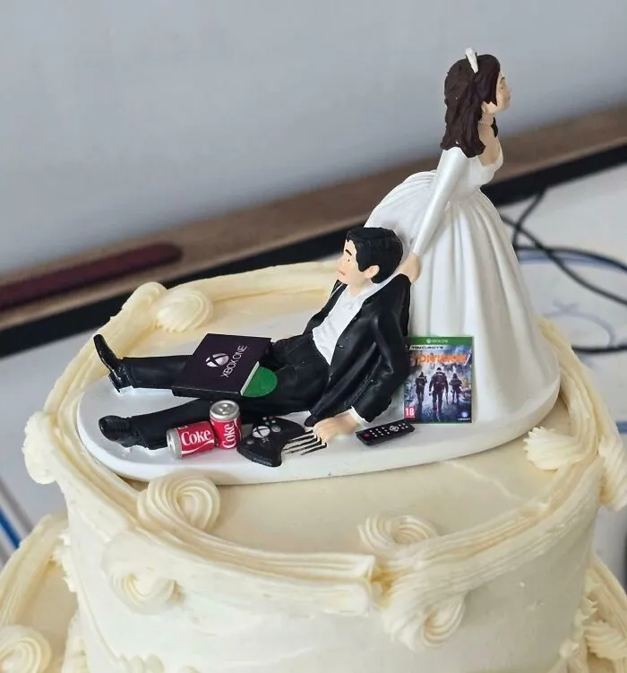 Wedding cake topper featuring bride pulling groom with gaming accessories