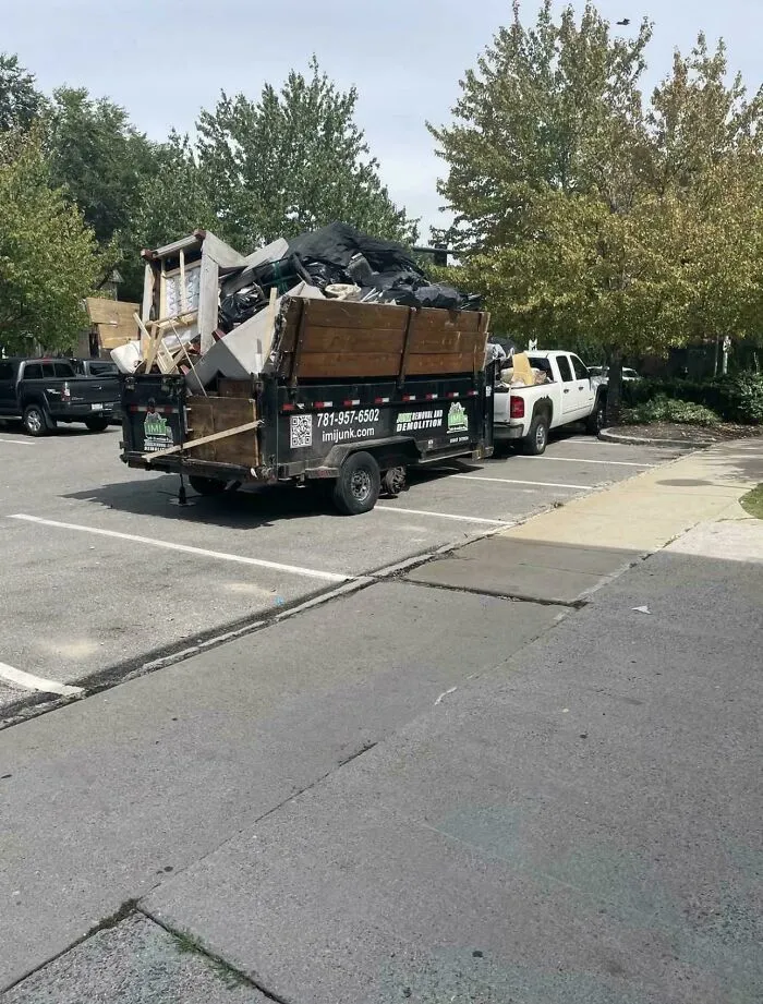 An overloaded junk removal trailer parked with missing wheels, showing a severe case of towing gone wrong.