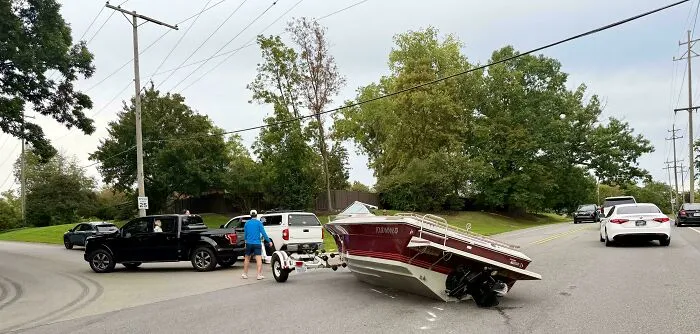 A motorboat fallen off its trailer and lying sideways on the road, showing an example of towing gone wrong.