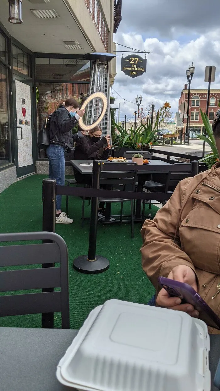 Influencers using ring lights to film food at an outdoor public restaurant patio.