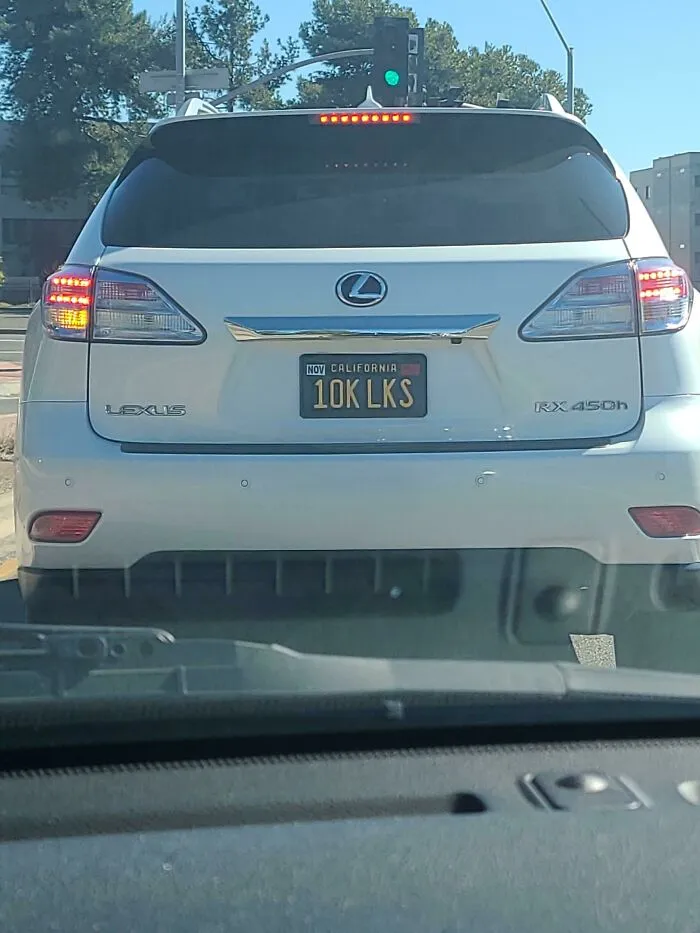 A rear view of a white Lexus car in public spaces featuring a custom California vanity license plate that reads 10K LKS.