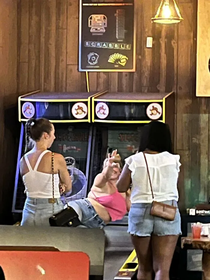 Woman lying on Skee-Ball machine as influencers turn public spaces into photoshoots.