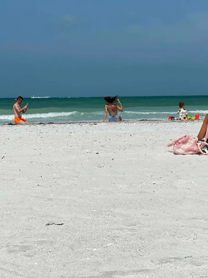 Woman posing on a public beach while a man takes photos, using public spaces as a personal content studio