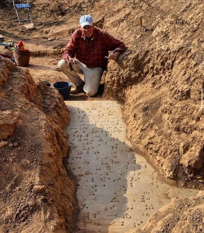 Archaeologist kneeling beside excavated cuneiform inscription carved into ancient stone.